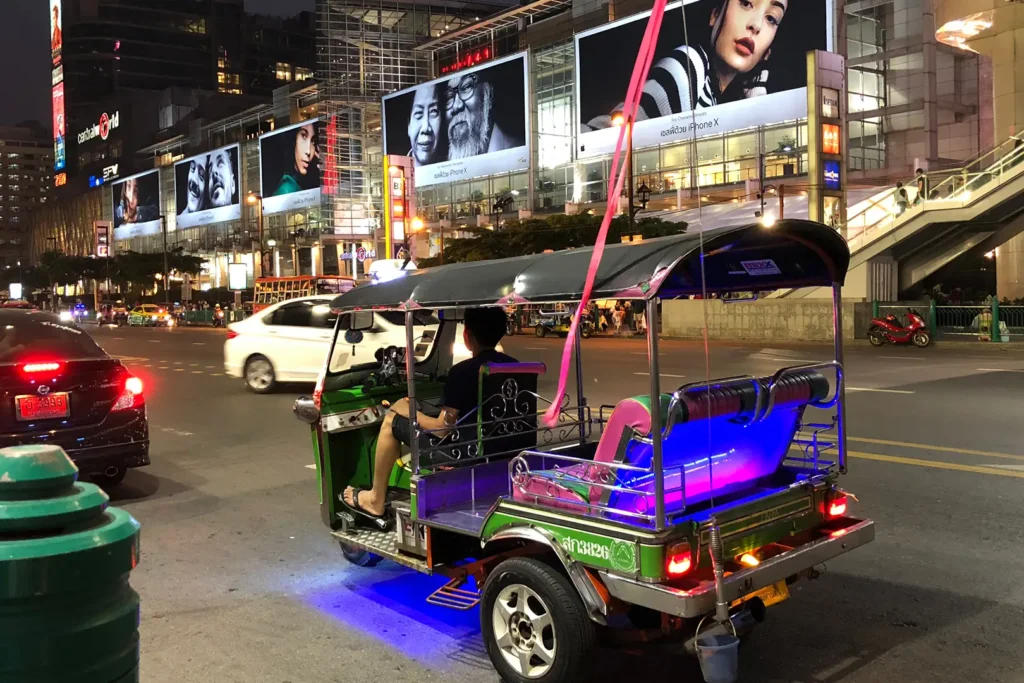 Tuk-tuk illuminé de néons roses et bleus la nuit devant le centre commercial CentralWorld à Bangkok