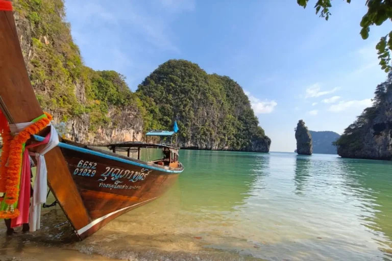 Long-tail boat amarré dans une crique aux eaux émeraude de la baie de Phang Nga, piton karstique en arrière-plan