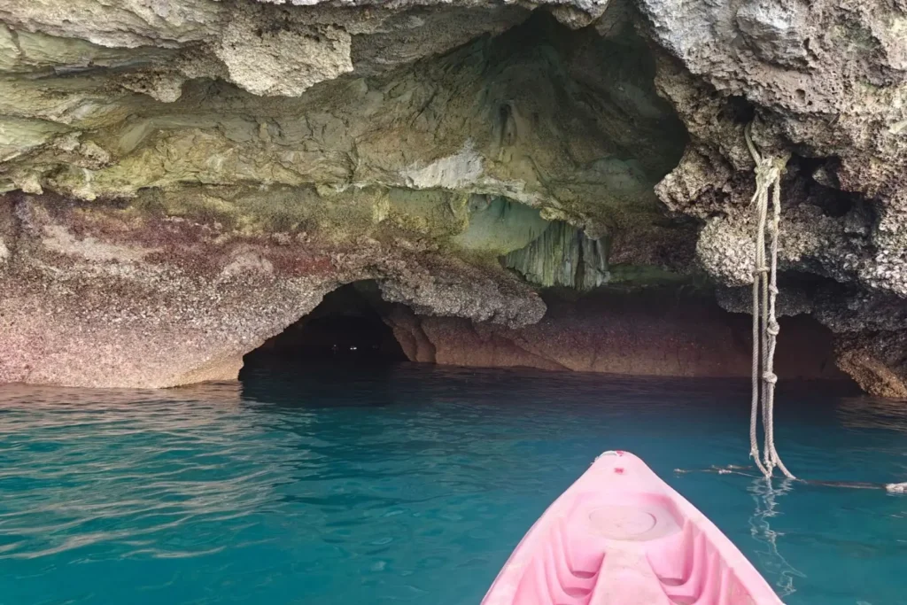 Kayak rose à l'entrée de la grotte d'Émeraude, eaux turquoise sous la voûte rocheuse de Koh Mook