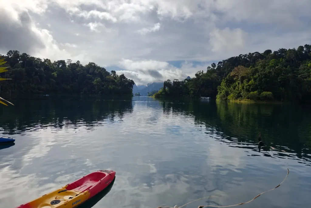 Kayak coloré au premier plan sur les eaux calmes du lac Cheow Lan, entouré de falaises calcaires et d'une forêt tropicale dense, parc national de Khao Sok.