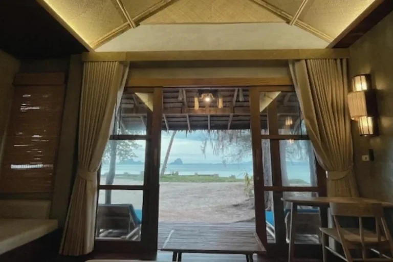 Essence du Sud 33 Vue depuis la chambre du Coco Cottage sur la mer turquoise de Koh Ngai à travers les grandes portes vitrées en bois ouvrant sur la plage, éco-resort en première ligne