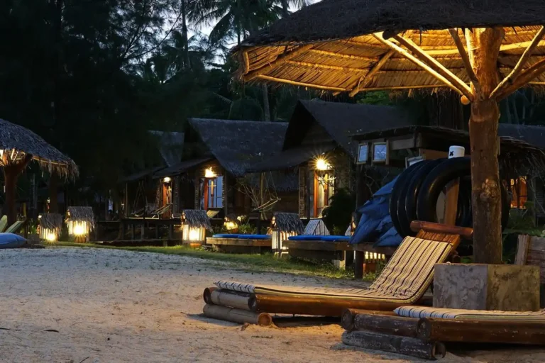 Essence du Sud 30 Rangée de bungalows à toit de chaume illuminés par des lanternes la nuit sur la plage de sable blanc de l'éco-resort Coco Cottage, Koh Ngai