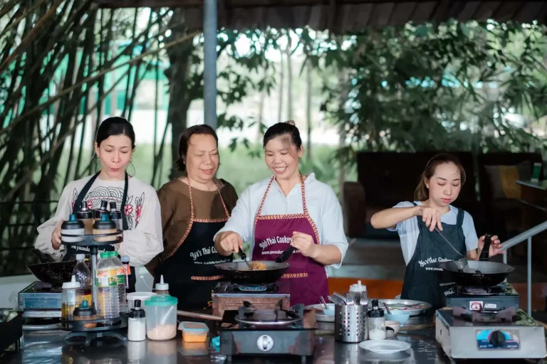 Quatre femmes en tabliers Yaa's Thai Cookery School cuisinent ensemble au wok lors d'un cours de cuisine thaïlandaise à Ao Nang, Krabi